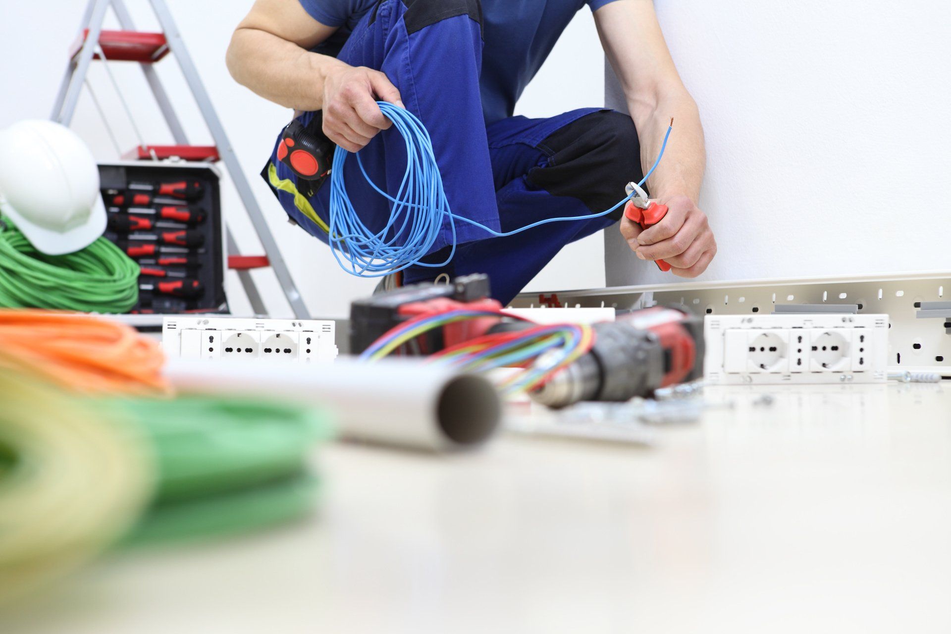 An electrician is kneeling down while working on a wall.