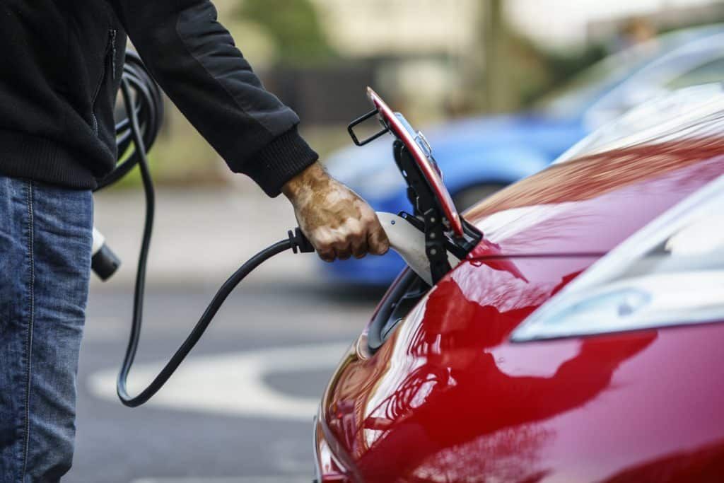A man is charging an electric car in a parking lot. A man is charging an electric car in a parking lot.