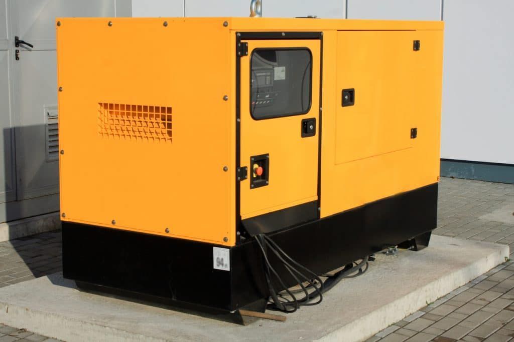 A yellow and black generator is parked in front of a building. A yellow and black generator is parked in front of a building.