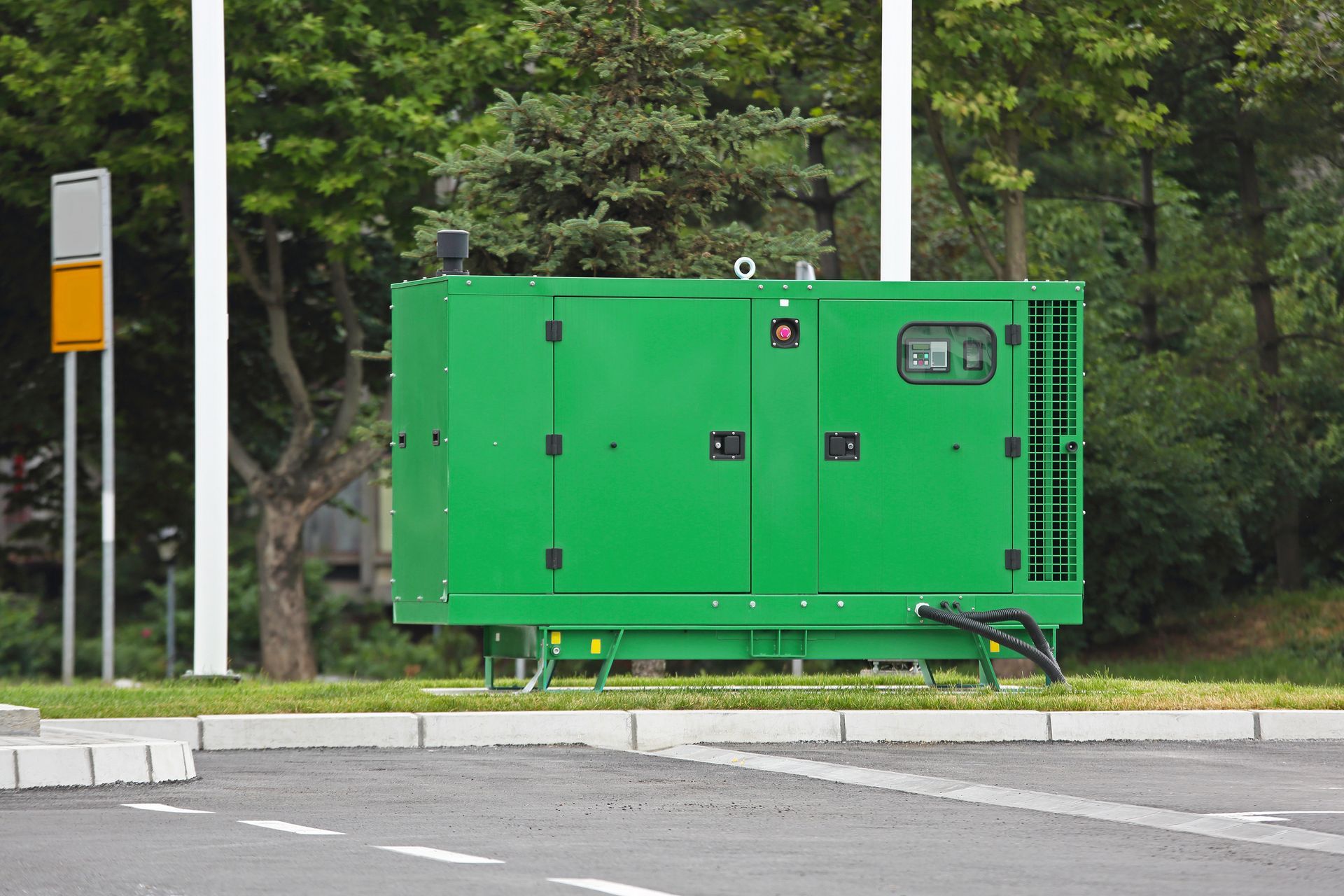 Green industrial generator on a grassy area, next to a road and trees. Green industrial generator on a grassy area, next to a road and trees.