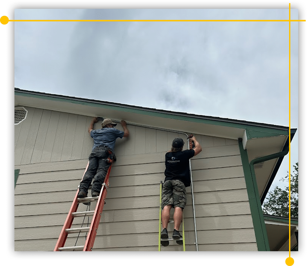 Two men are working on the side of a house on a ladder. Two men are working on the side of a house on a ladder.