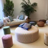 Bright lounge with cushioned ottomans, patterned bench, and potted plants against a beige wall