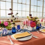 Elegant banquet table with coral tablecloth, flowers, blue glasses, and sunset-lit windows
