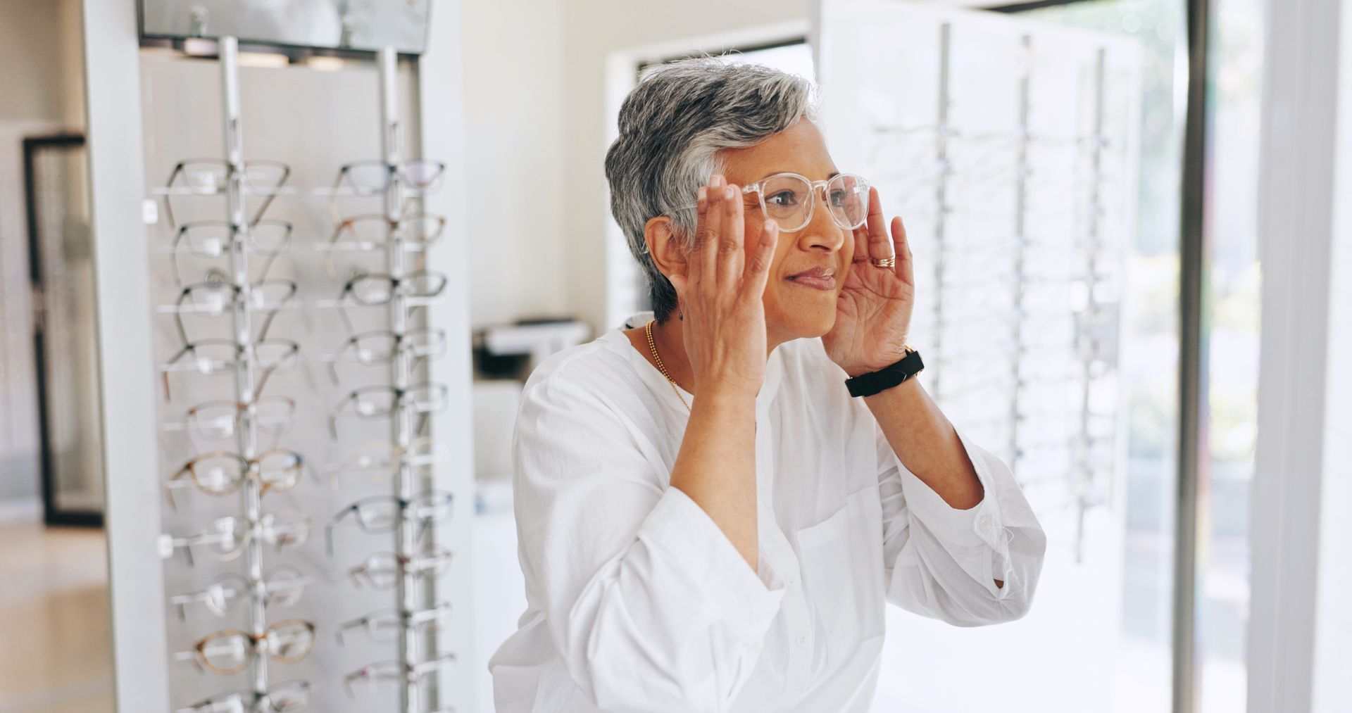 Person adjusting eyeglasses in a bright optical store, with rows of glasses in the background Person adjusting eyeglasses in a bright optical store, with rows of glasses in the background