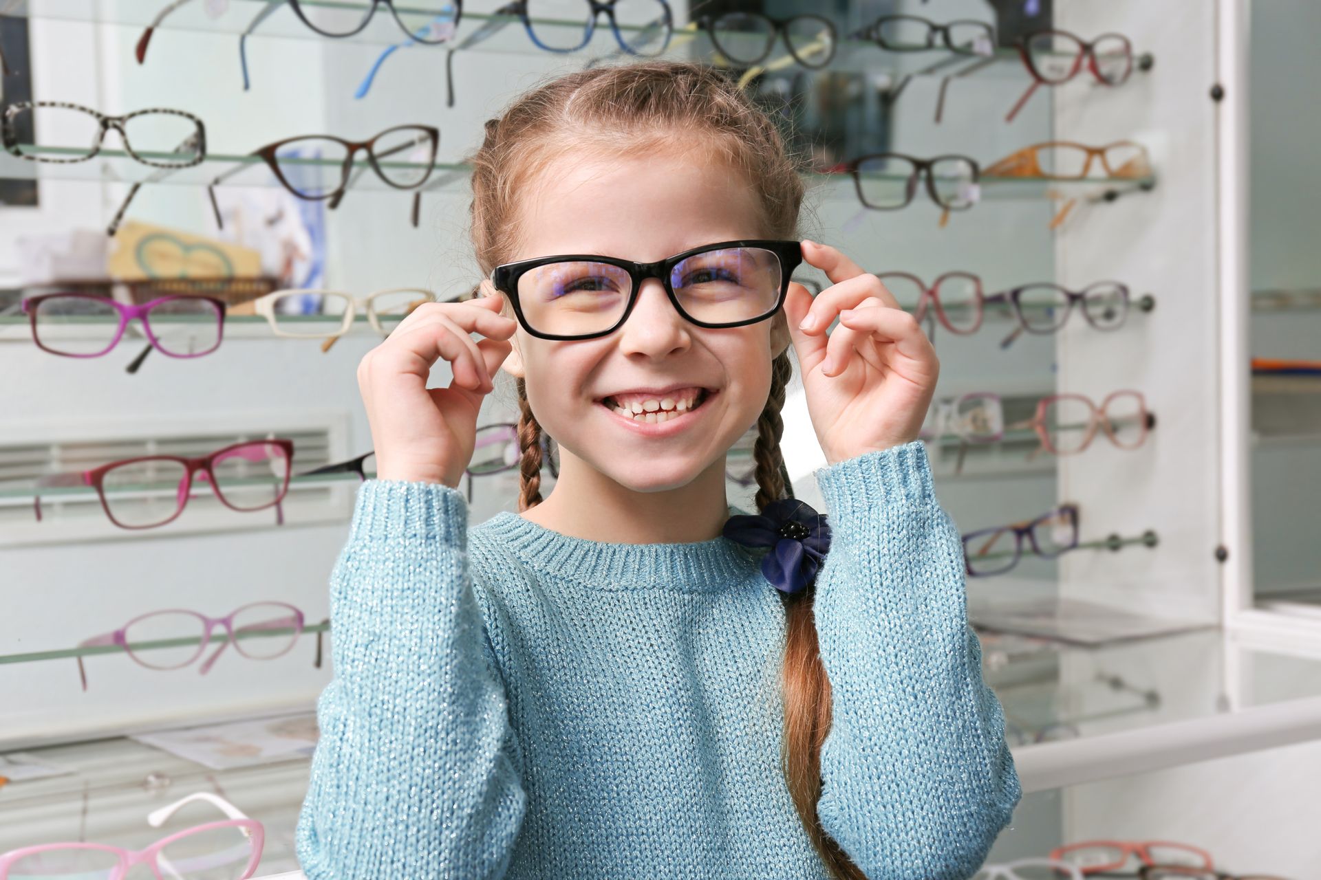Child trying on black eyeglasses in an optical shop, smiling beside rows of colorful frames Child trying on black eyeglasses in an optical shop, smiling beside rows of colorful frames