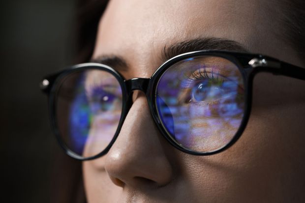 Close-up of a person wearing glasses, with blue reflections on the lenses