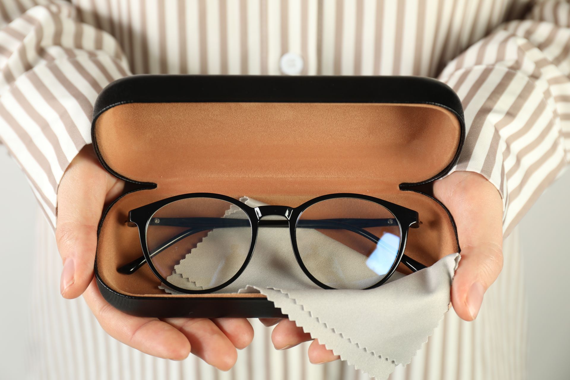 Hands holding an open glasses case with black eyeglasses and a cleaning cloth inside Hands holding an open glasses case with black eyeglasses and a cleaning cloth inside