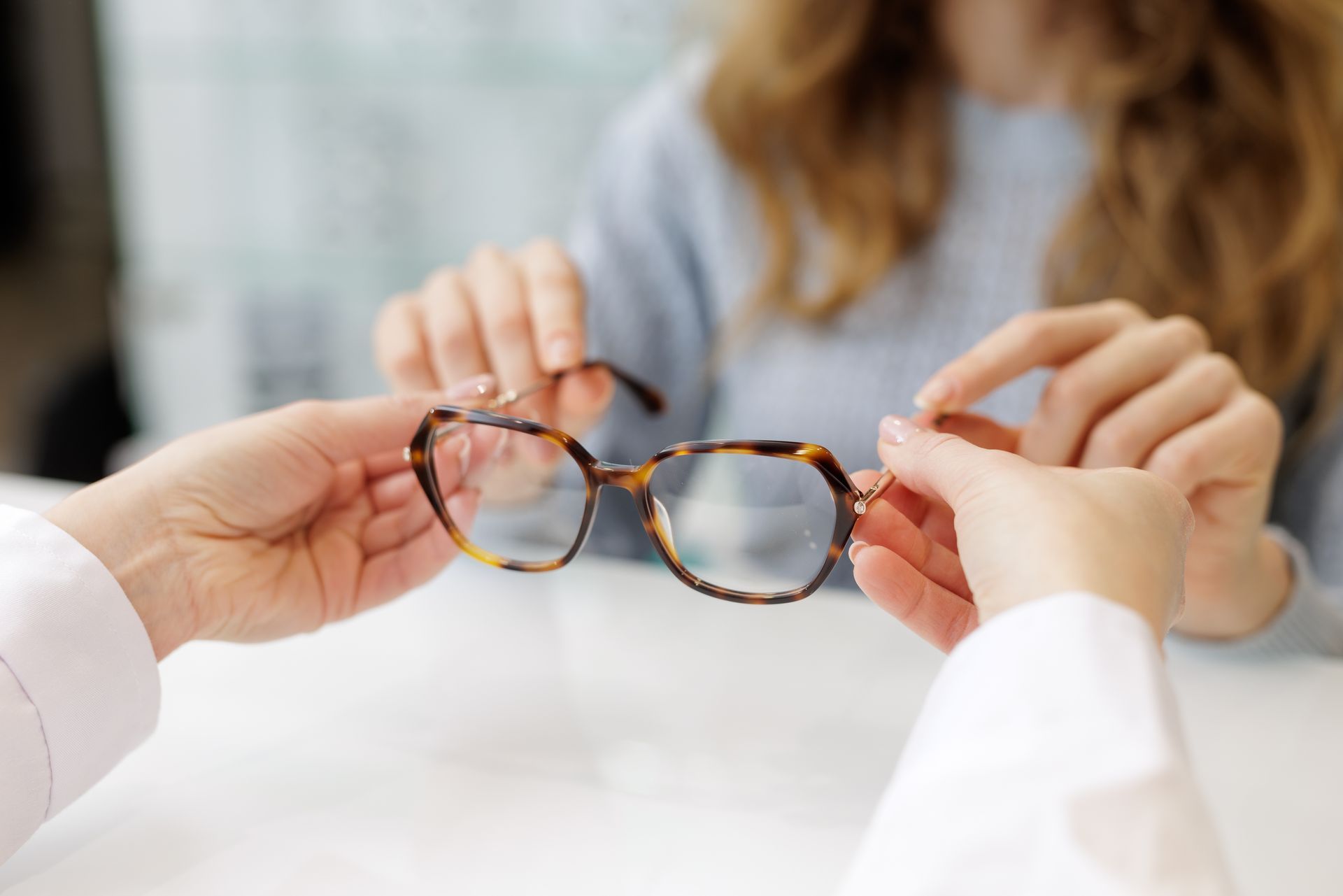 Hands holding tortoiseshell eyeglasses in a bright office setting Hands holding tortoiseshell eyeglasses in a bright office setting
