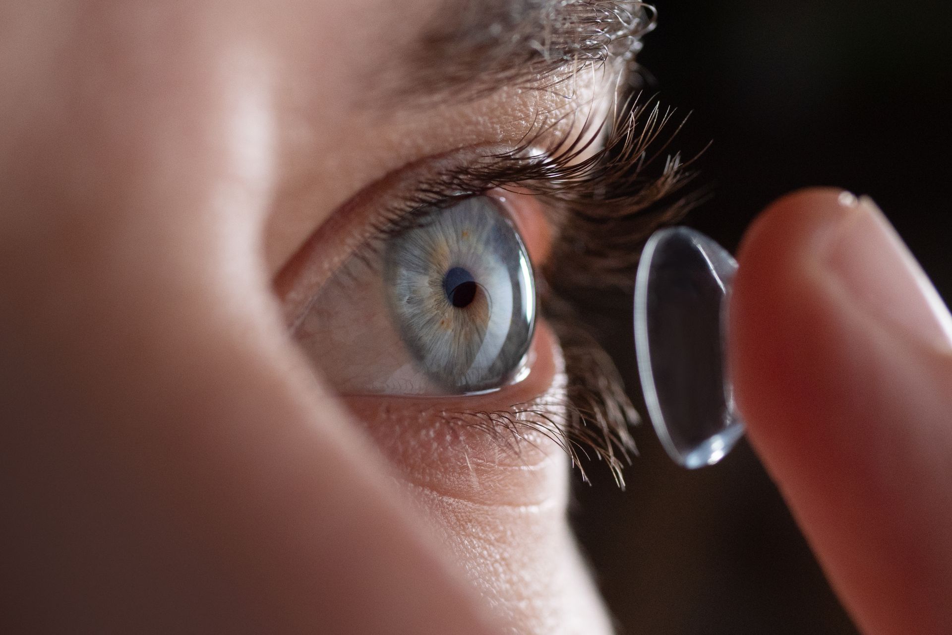 Close-up of an eye with a contact lens being held near it by a fingertip
