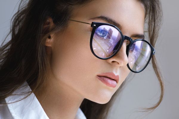 Close-up of a woman wearing round glasses, looking to the side against a gray background