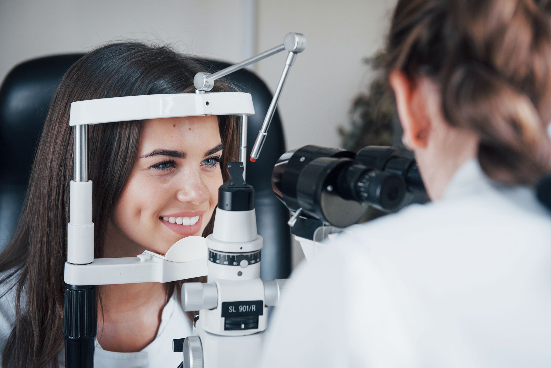 Patient undergoing an eye exam with a slit lamp while an optometrist checks her vision