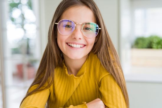 Smiling woman in yellow sweater and glasses in a bright room