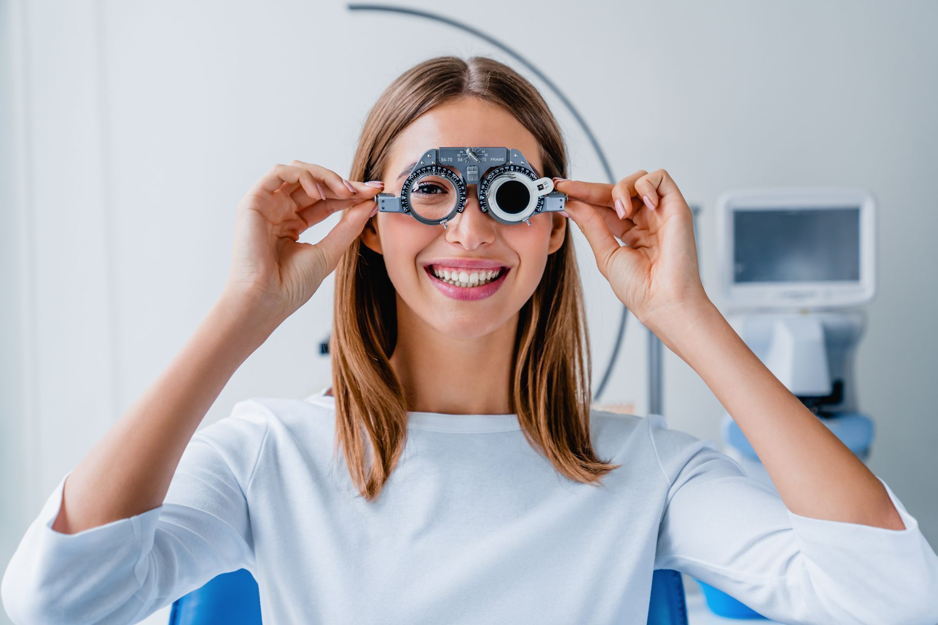 Woman smiling while adjusting glasses in a bright office, with a computer in the background