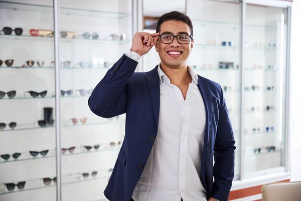 Man smiling in a suit adjusting glasses in a sunglass store