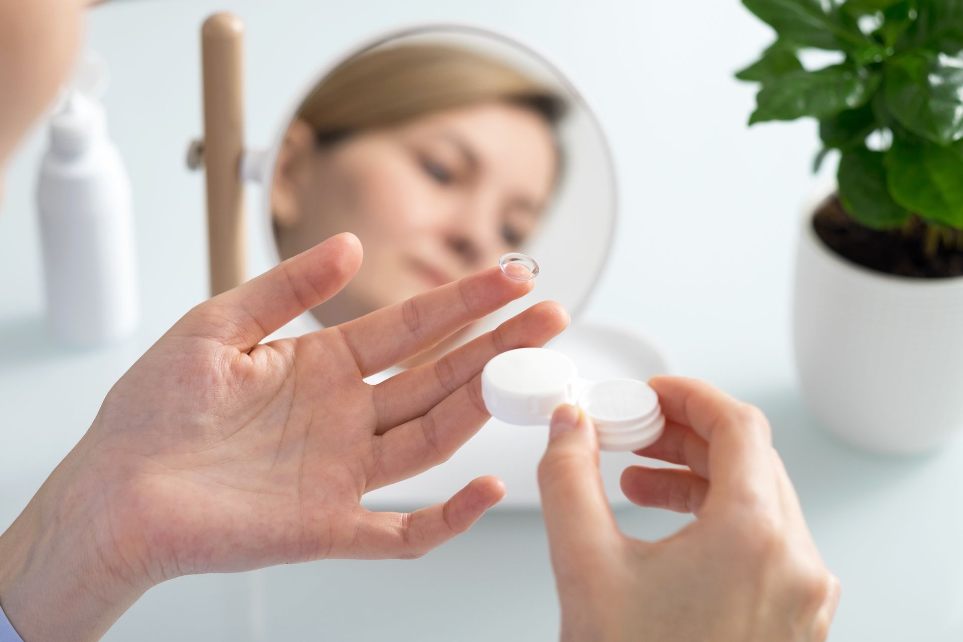 Hands holding a contact lens case beside a blurred face on a bright bathroom counter Hands holding a contact lens case beside a blurred face on a bright bathroom counter