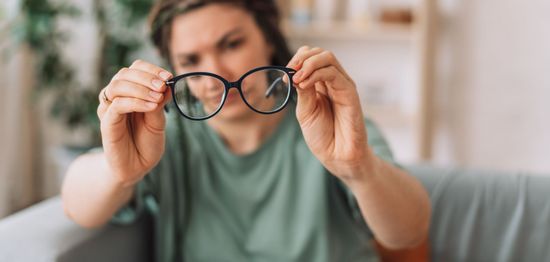 Person holding black eyeglasses up to their face in a softly lit indoor setting