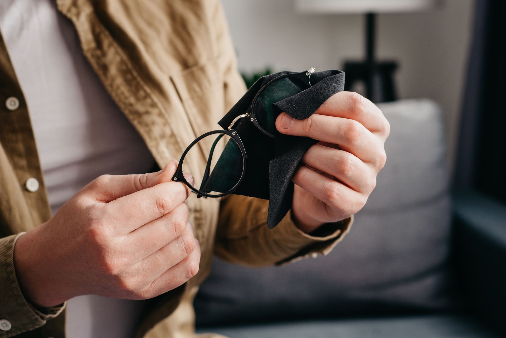 Hands adjusting a black face mask on a couch, with a beige shirt and gray pillow in the background Hands adjusting a black face mask on a couch, with a beige shirt and gray pillow in the background