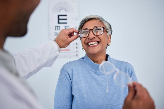 Optometrist adjusting glasses on a smiling patient during an eye exam