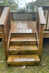 Weathered wooden deck stairs with railings leading to a wet porch in a backyard.