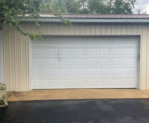 White double garage door on a beige house with a wet driveway and overhanging tree branches.