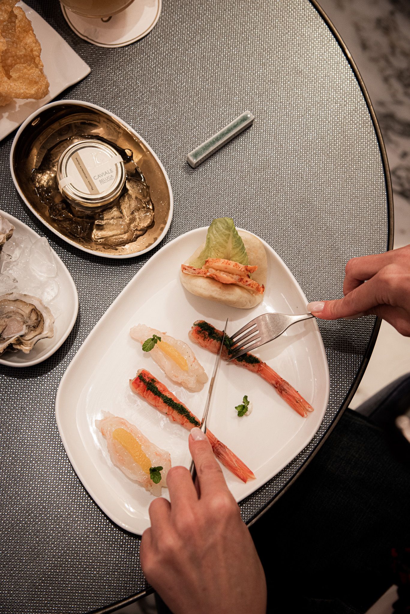 In un ristorante scarsamente illuminato, una persona usa forchetta e coltello per mangiare un piatto di antipasti misti a base di frutti di mare.