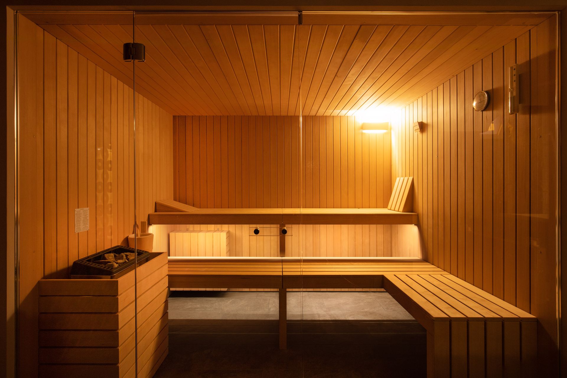 Una moderna sauna in legno con panche a più livelli, stufa in pietra e illuminazione interna calda.