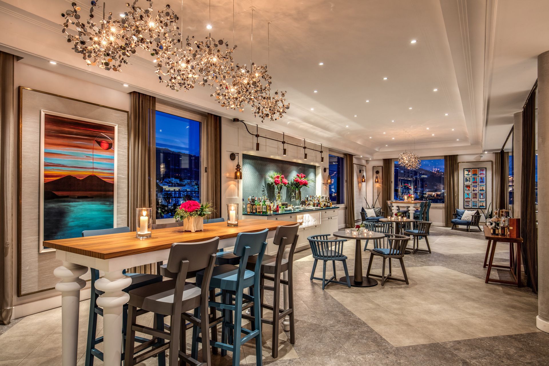 Elegant restaurant lounge with chandeliers, bar seating, and tables in a warmly lit interior.
