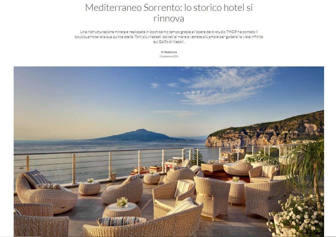 A sunlit hotel terrace in Sorrento featuring wicker furniture overlooking the ocean with Mount Vesuvius in the distance.