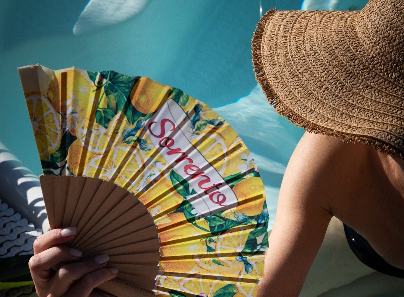 Una persona con un cappello di paglia tiene in mano un ventaglio giallo decorato con limoni e la scritta