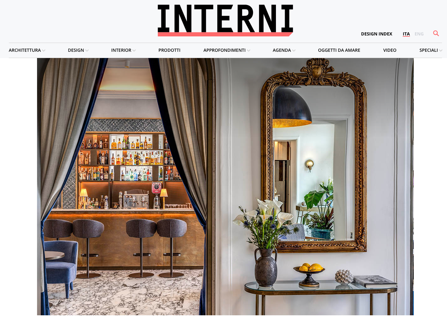 A bar interior visible through draped curtains next to an ornate gold mirror on a wall with a vase and side table.