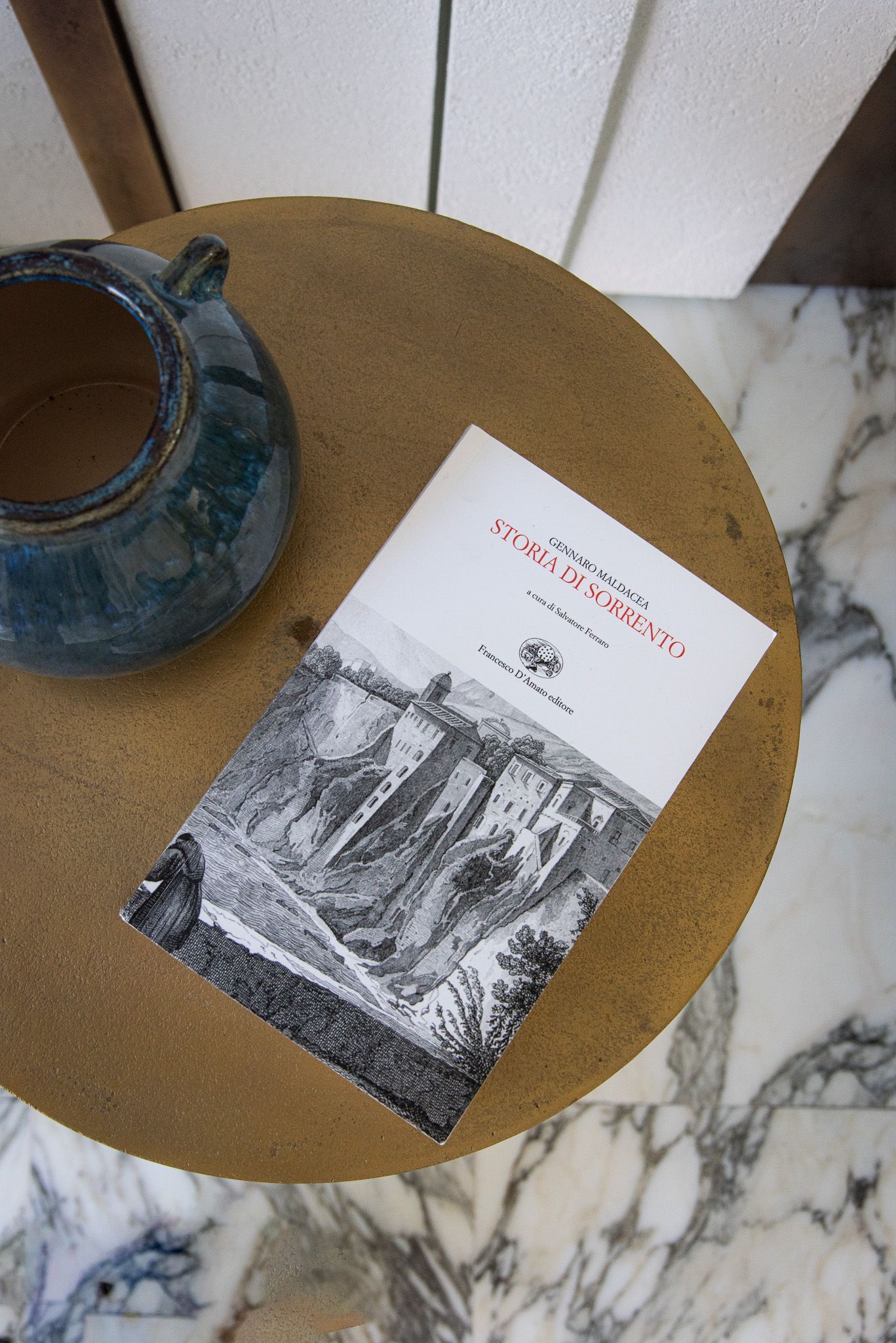 A small book with a black-and-white landscape cover resting on a textured, round table next to a blue ceramic pot.