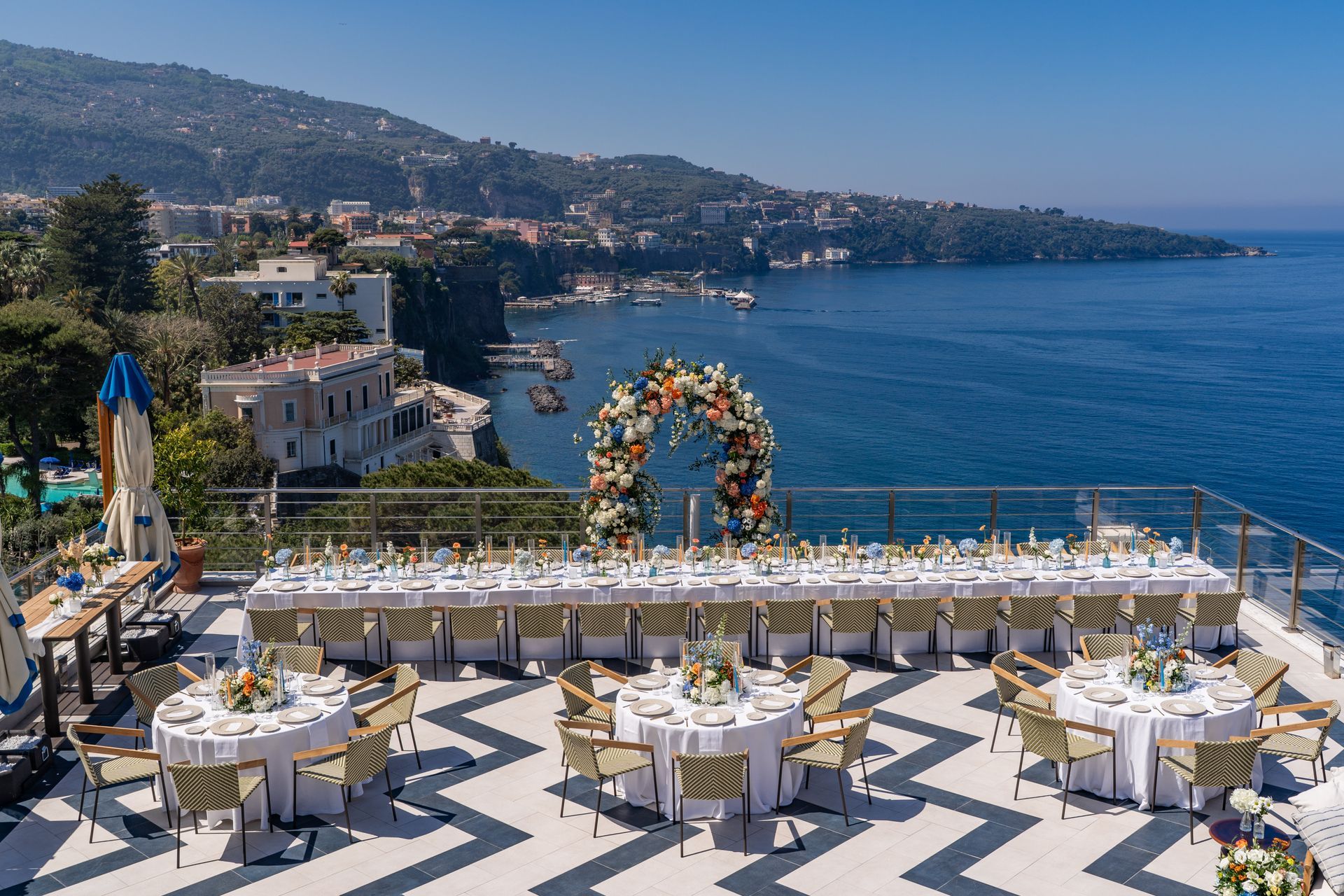 Terrazza sul mare allestita per un matrimonio con tavoli bianchi, arco floreale e vista sul mare