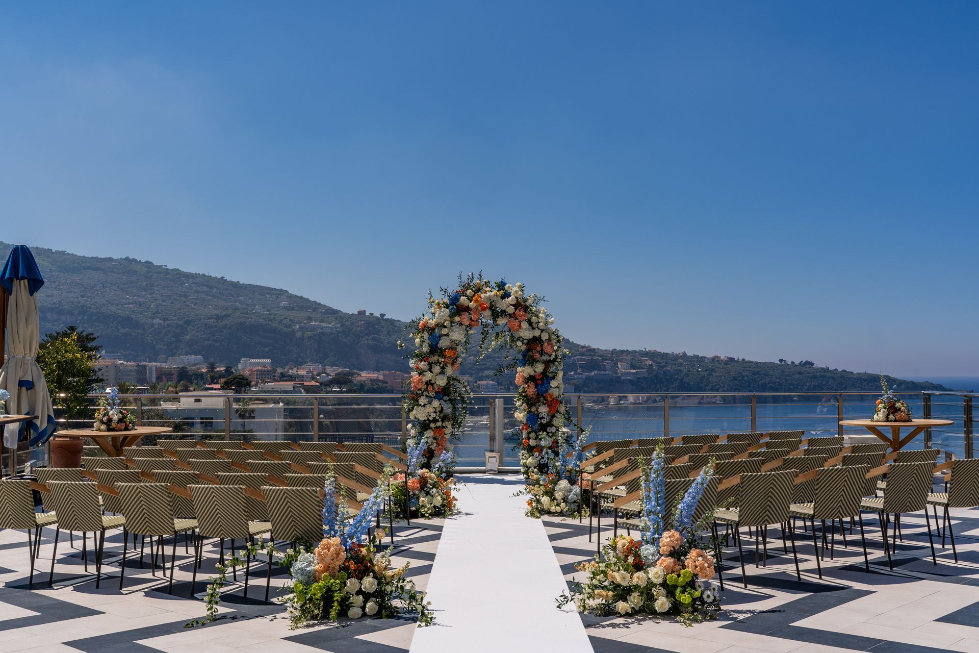 Outdoor wedding aisle with white runner and floral arch overlooking a blue bay 