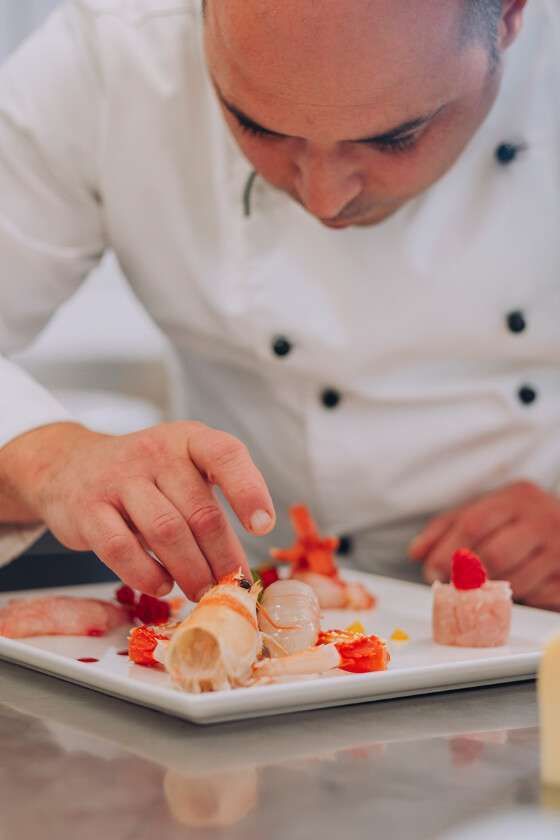 A chef in a white uniform carefully garnishes an elegant, gourmet seafood dish on a white plate.