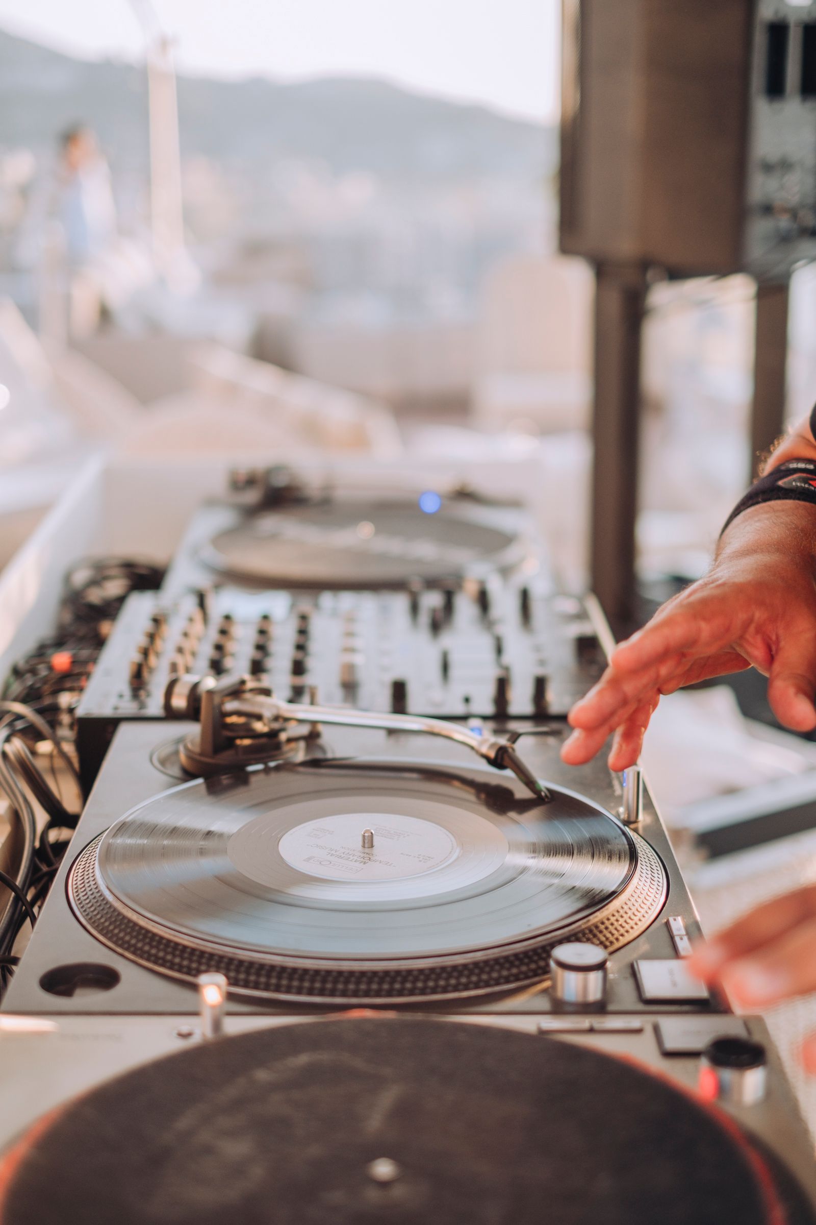 Primo piano della mano di una persona che sistema un disco in vinile su un giradischi da DJ durante un evento all'aperto.