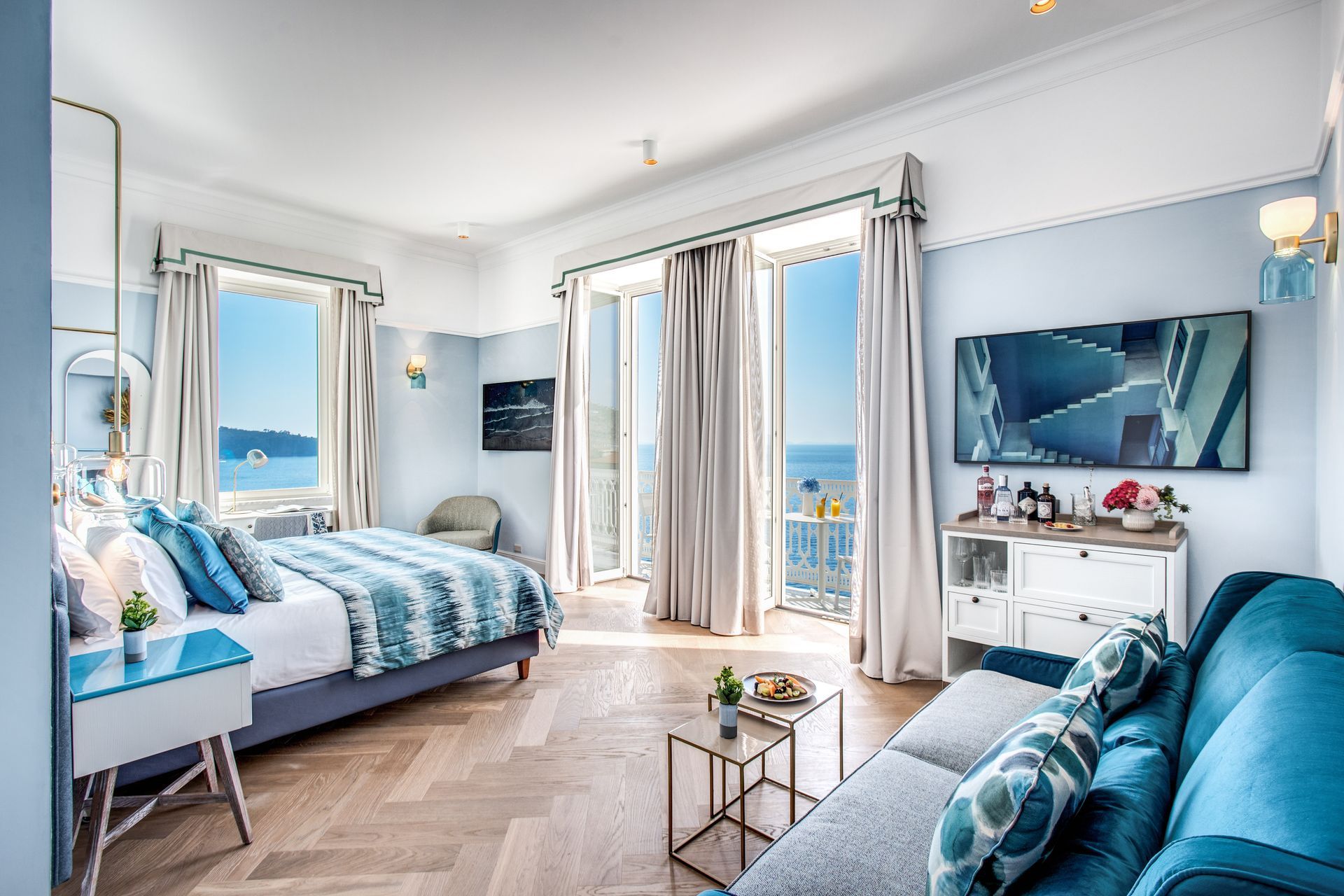 Una camera d'albergo luminosa e moderna, con letto, divano blu e un'ampia finestra che offre una splendida vista sull'oceano.