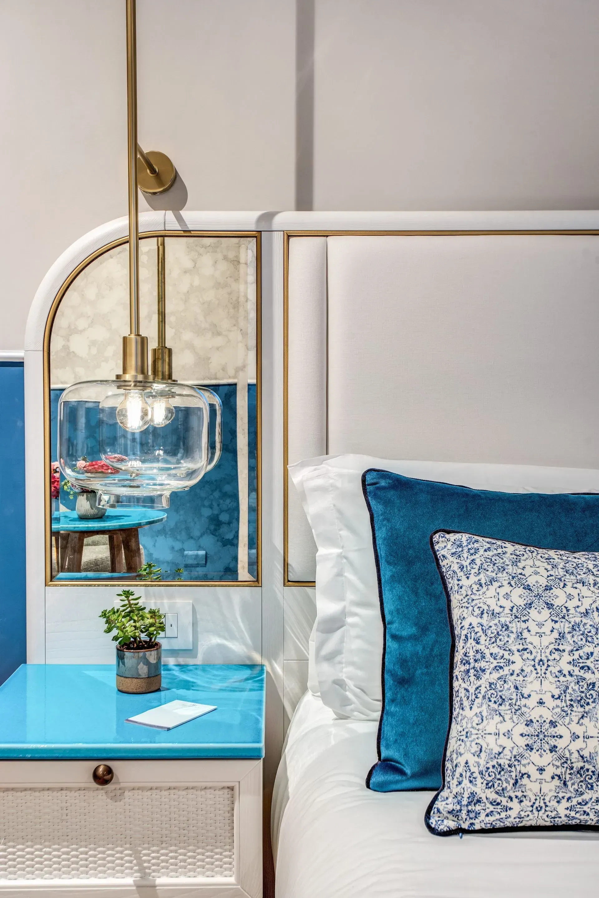 Three pump bottles—light blue, white, and dark blue—sit in a tall, gold-framed black shelf against a geometric background.