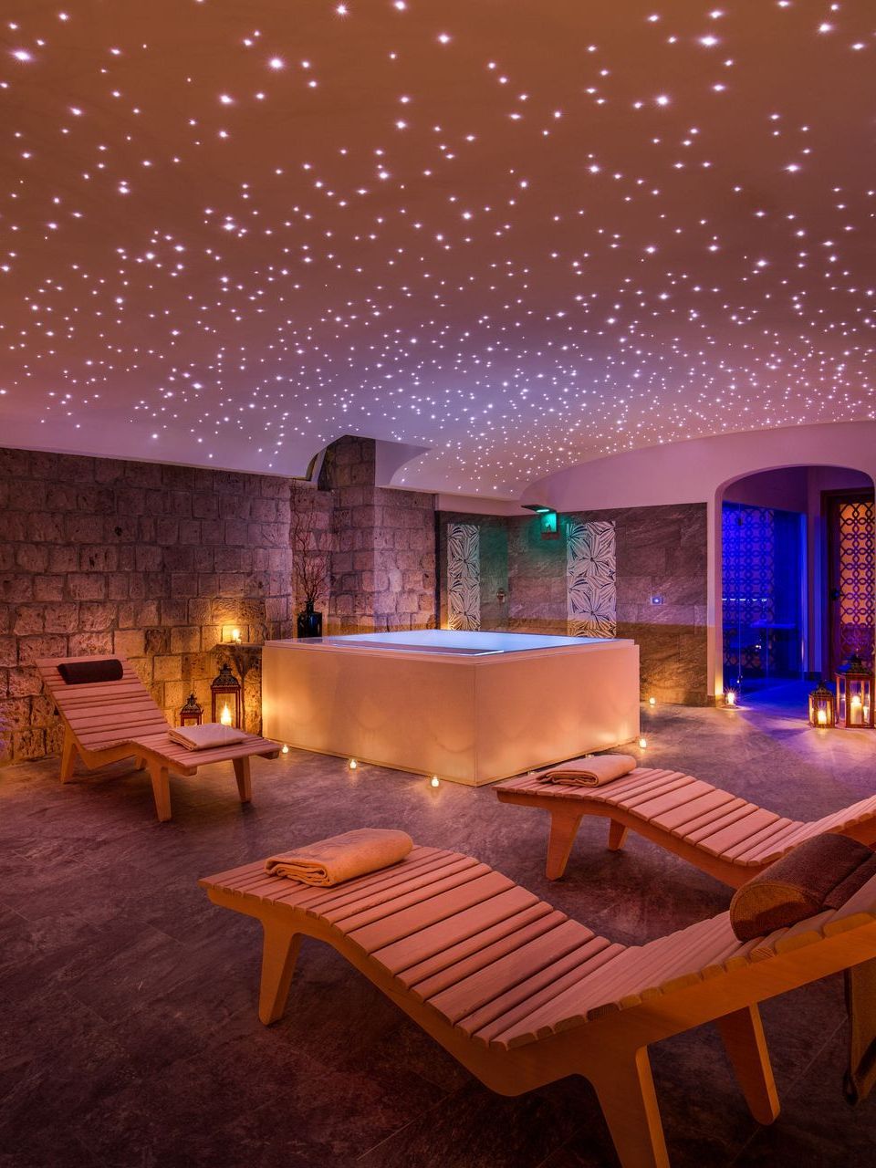 A spa room featuring a square hot tub, three wooden lounge chairs, and a ceiling filled with tiny glowing starlights.