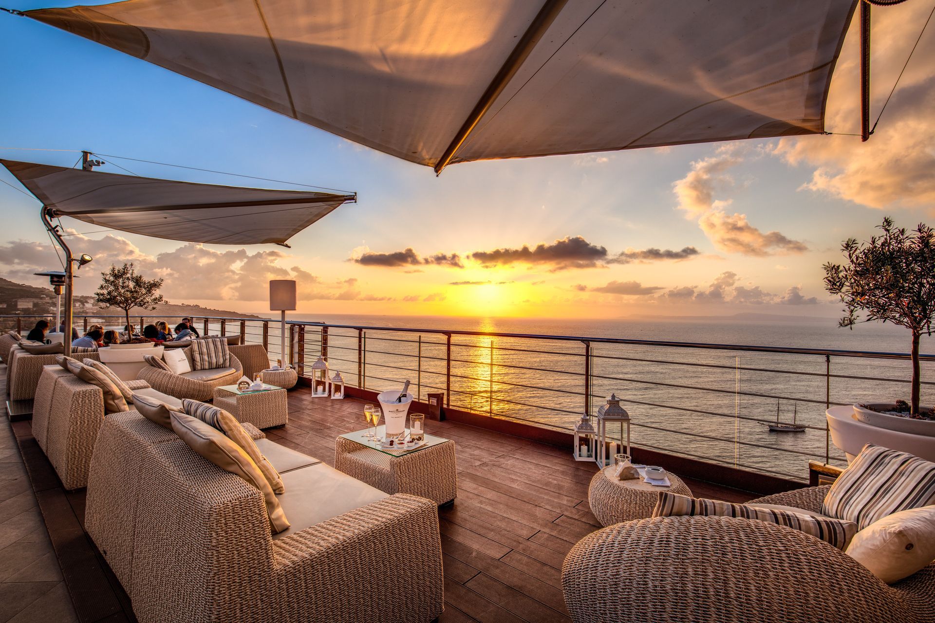 Un tramonto visto da una terrazza sul mare con lettini in vimini sotto gli ombrelloni, affacciata sull'oceano.