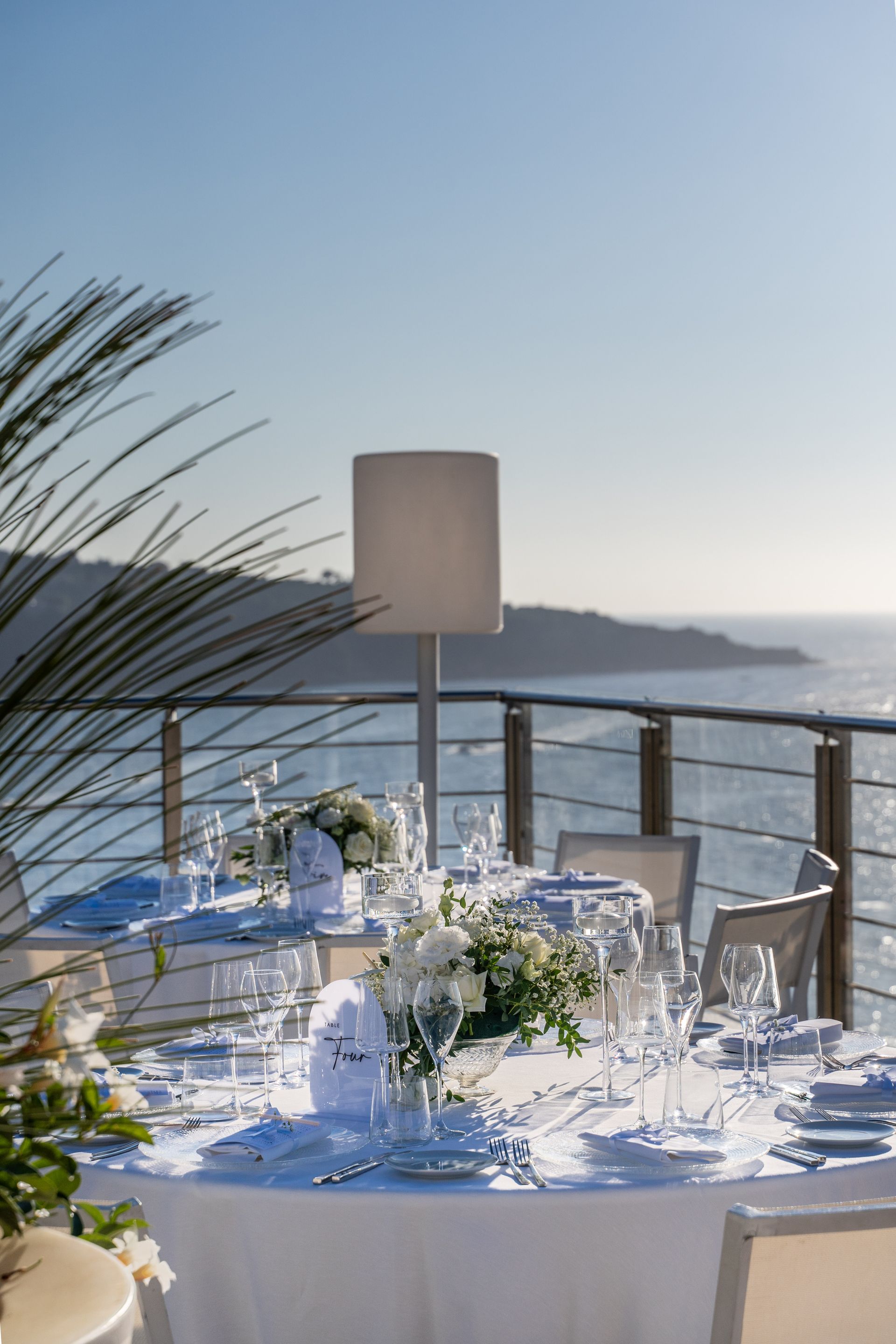 Eleganti tavoli apparecchiati per un evento all'aperto con vista sull'oceano in una giornata di sole.