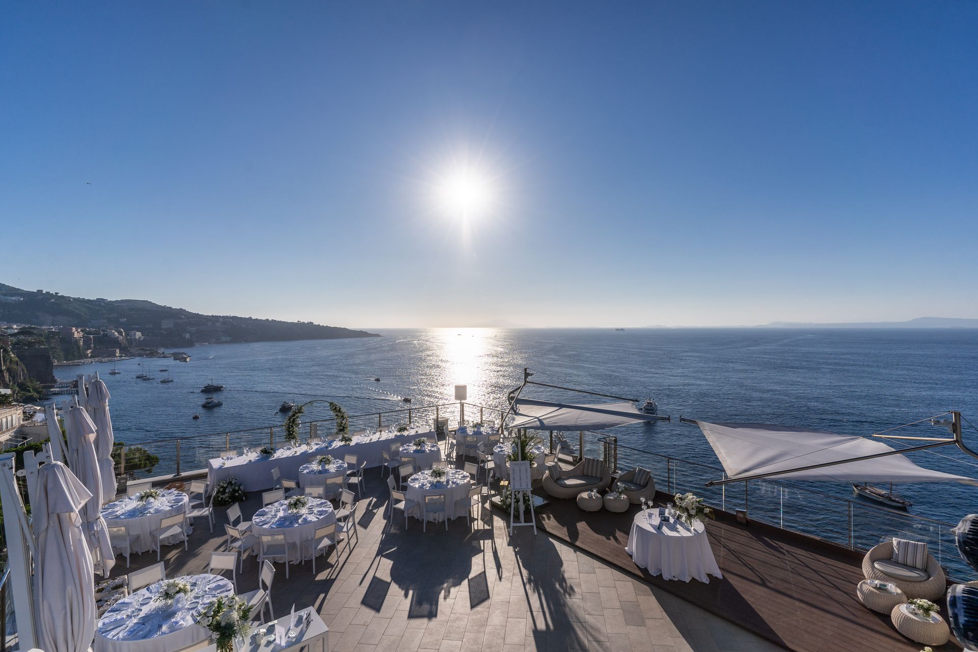 Una location per matrimoni all'aperto con tavoli bianchi affacciati sull'oceano sotto un cielo limpido e soleggiato.