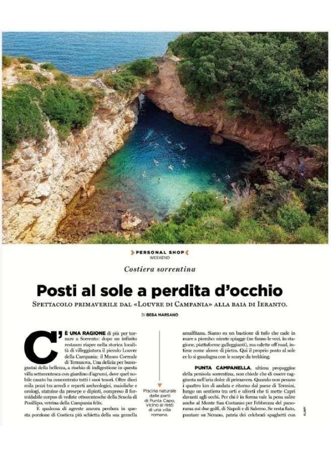 An aerial view of the emerald waters of Baia di Ieranto, nestled between rocky cliffs and lush green Mediterranean flora.