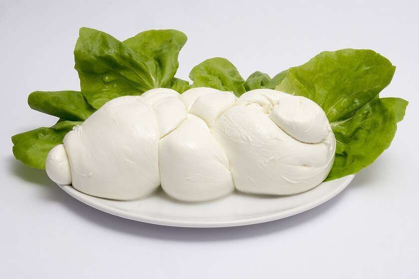 A large, knotted ball of white mozzarella cheese resting on a white plate atop a bed of fresh green lettuce leaves.