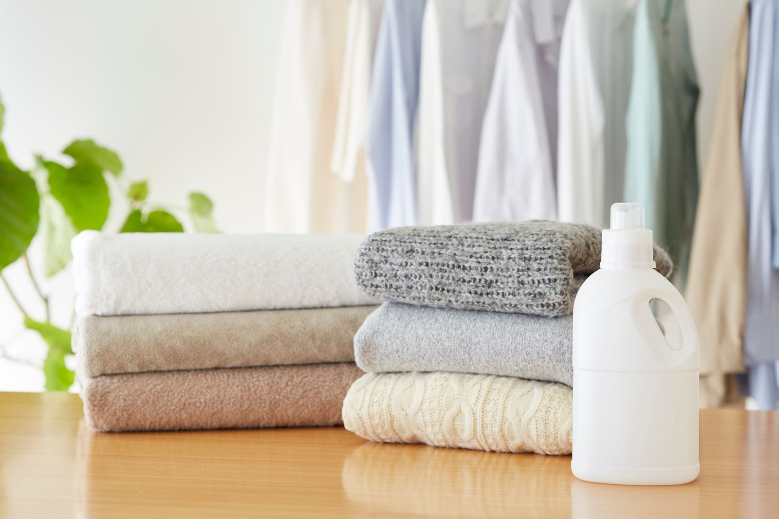 A stack of towels and a bottle of laundry detergent on a wooden table.