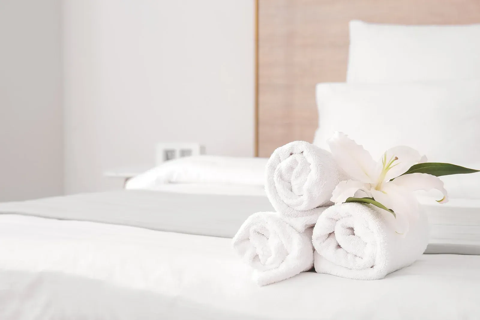 A bed with rolled towels and a flower on it.