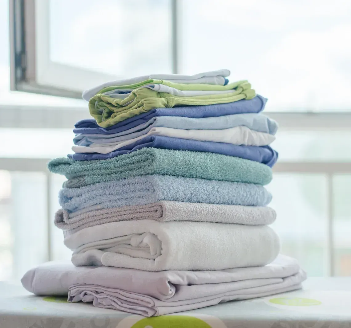A stack of towels sits on a table in front of a window
