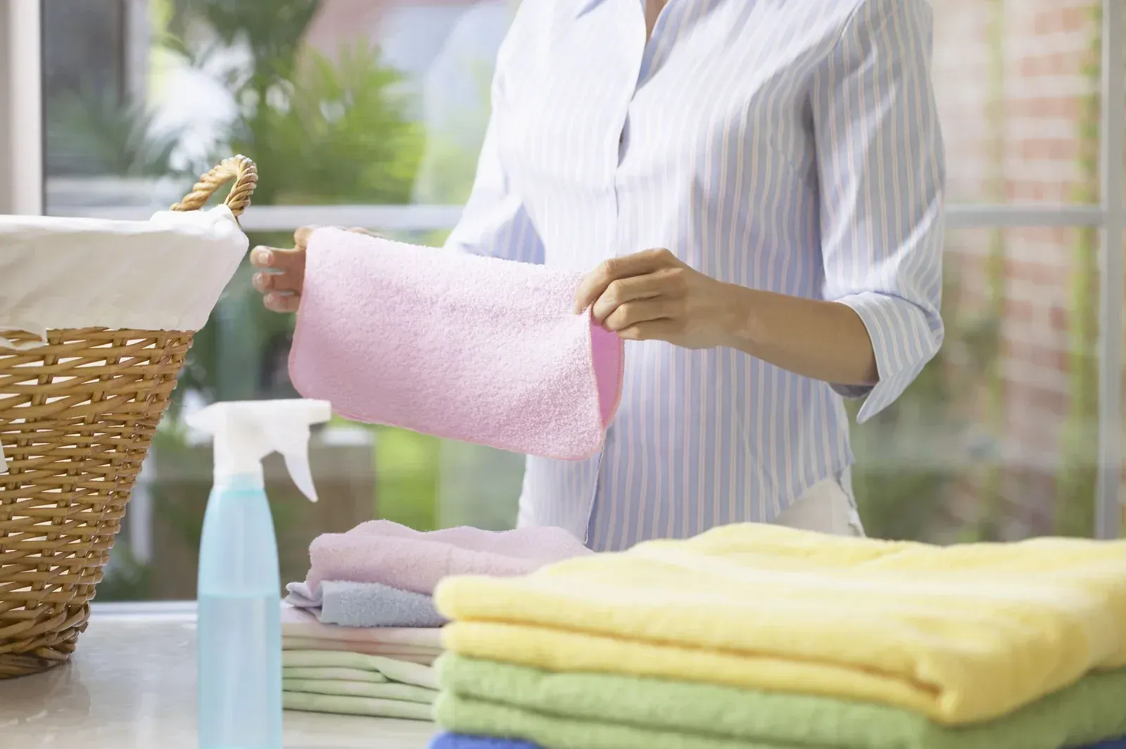 A woman is holding a pink towel in front of a stack of towels.