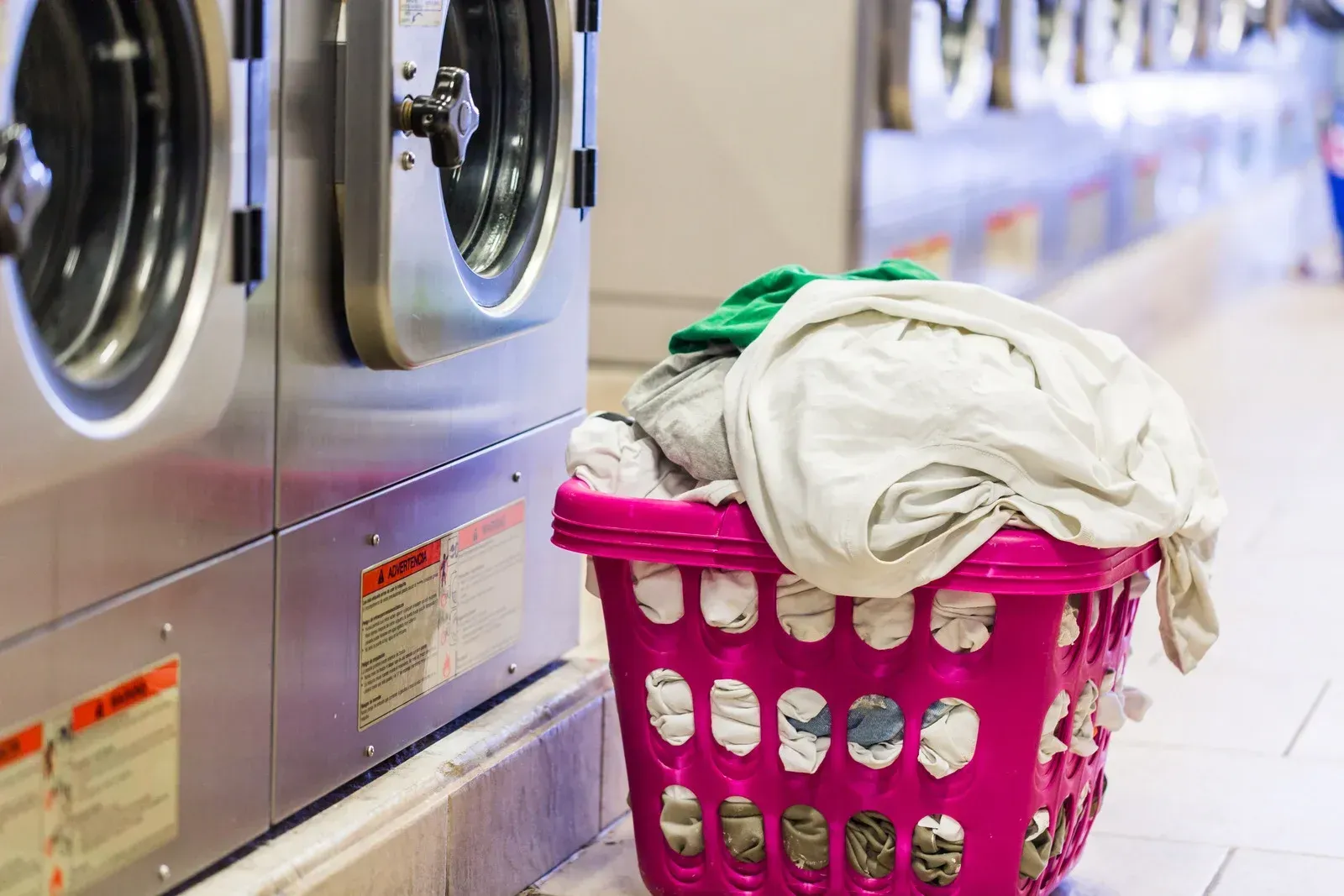 A pink laundry basket is filled with clothes in a laundromat.