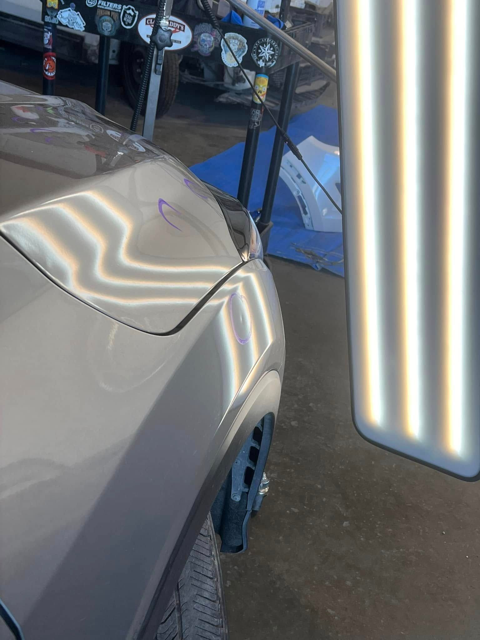 Car's front fender with a dent being inspected using lights in a shop.