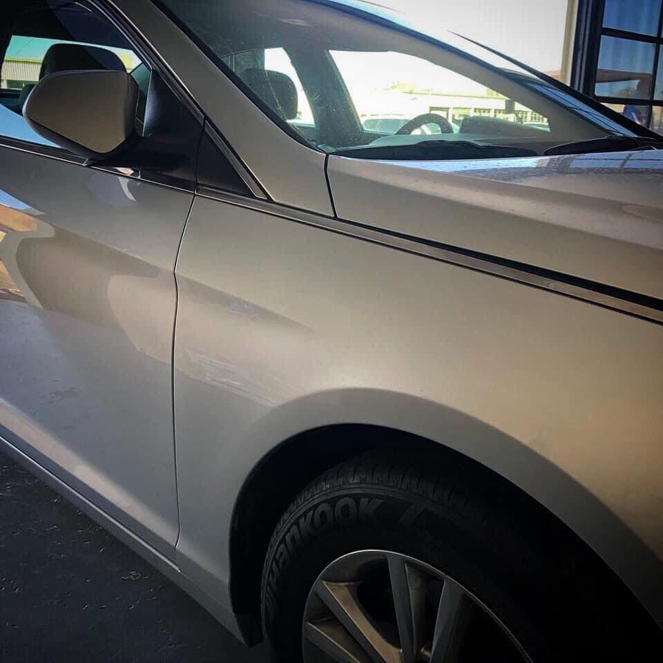 Silver car's front side, parked indoors. Shows tire, mirror, window, and black pinstripe along body.